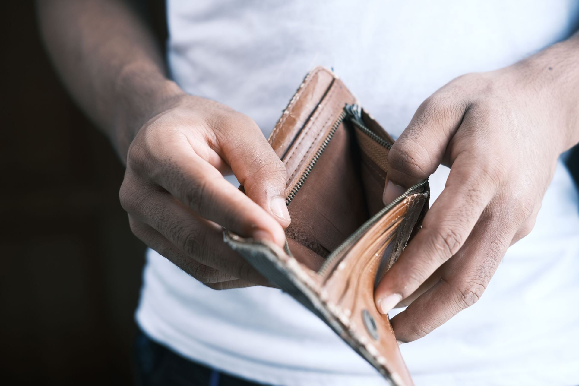Hands holding an open, mostly empty brown wallet against a white shirt