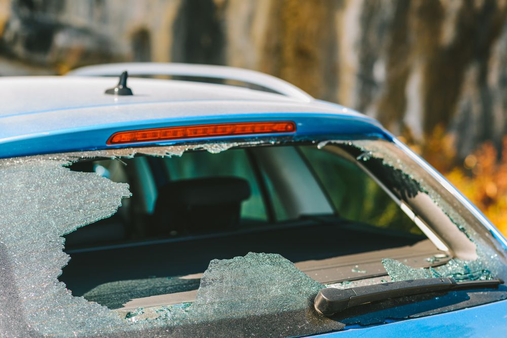 Blue car with shattered rear window and broken glass, parked outdoors