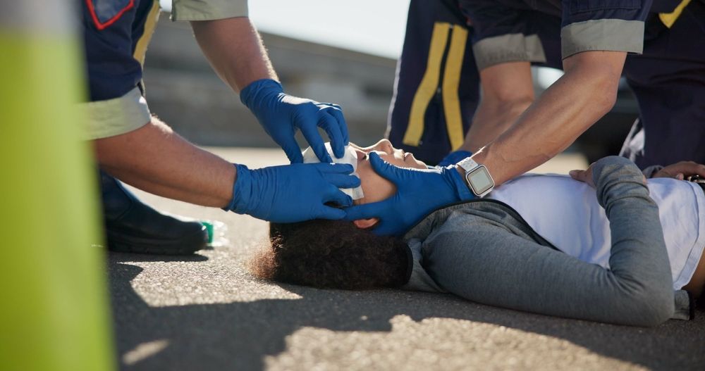 Paramedics in blue gloves perform CPR on a person lying on the road