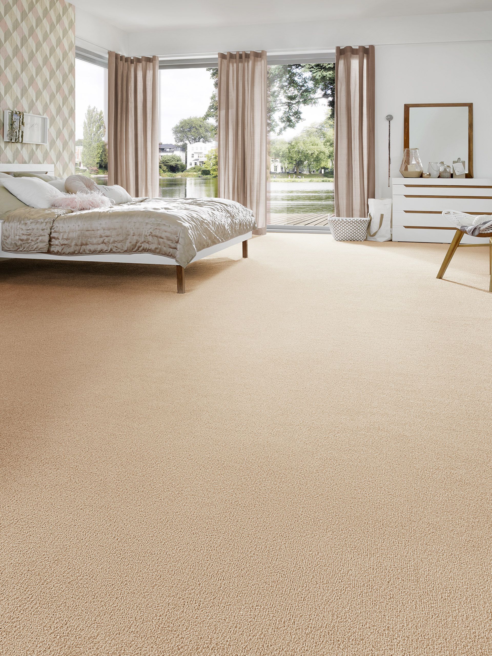 Chambre moderne avec moquette beige clair, un lit avec une literie moelleuse et de grandes fenêtres avec des rideaux descendant jusqu'au sol.