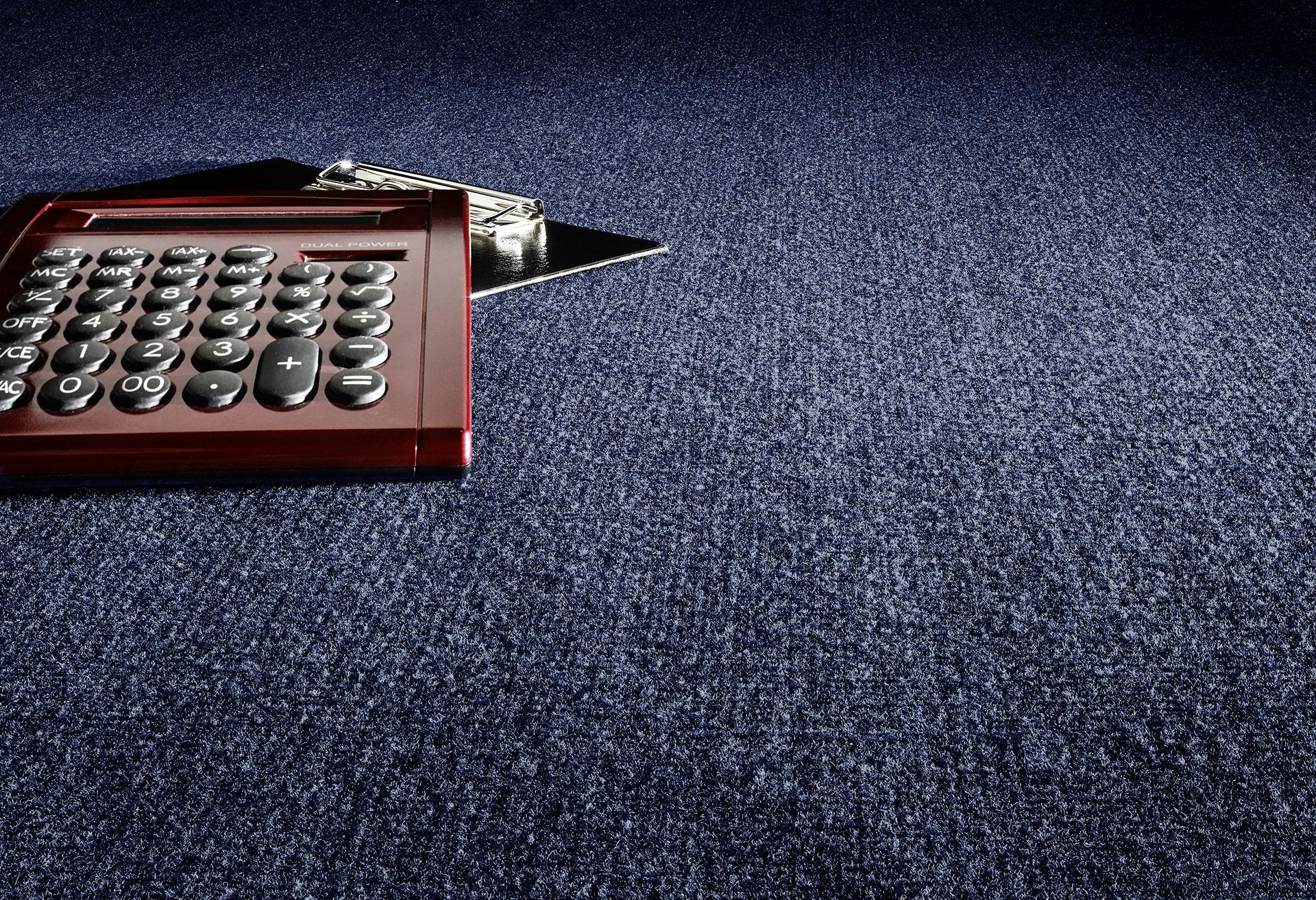 Une calculatrice rouge repose sur une moquette texturée bleu foncé.