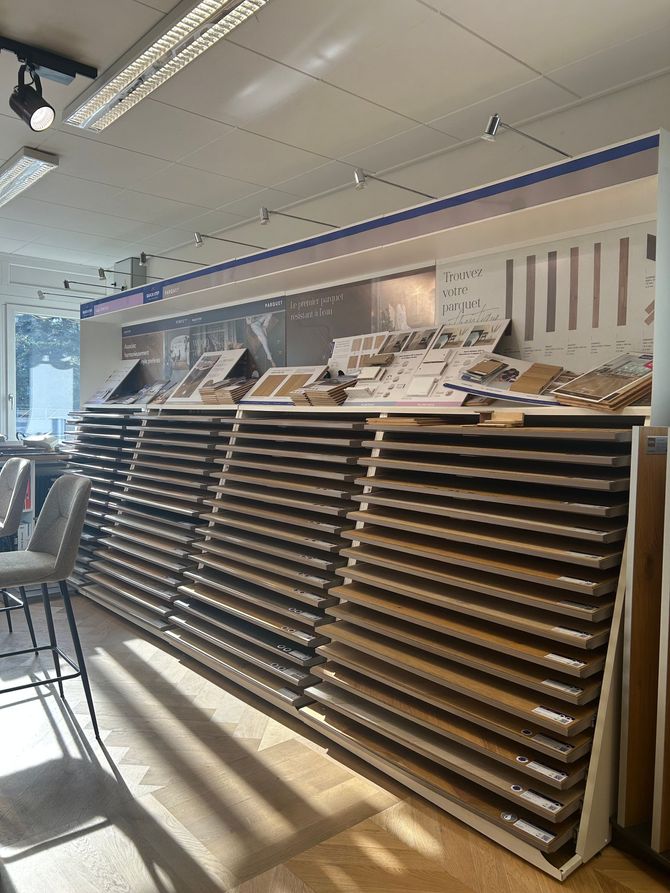 Un présentoir de salle d'exposition contenant de nombreux échantillons de revêtements de sol en bois, avec des images d'inspiration pour la décoration intérieure affichées au-dessus.