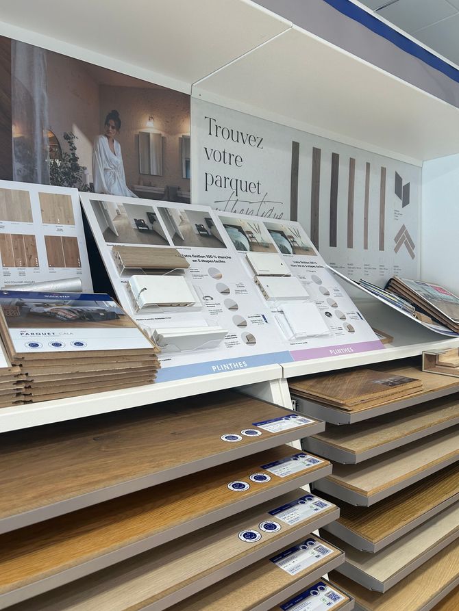 Un présentoir commercial mettant en valeur des échantillons de revêtements de sol, notamment des lames de bois et des brochures, sur fond de mur informatif.