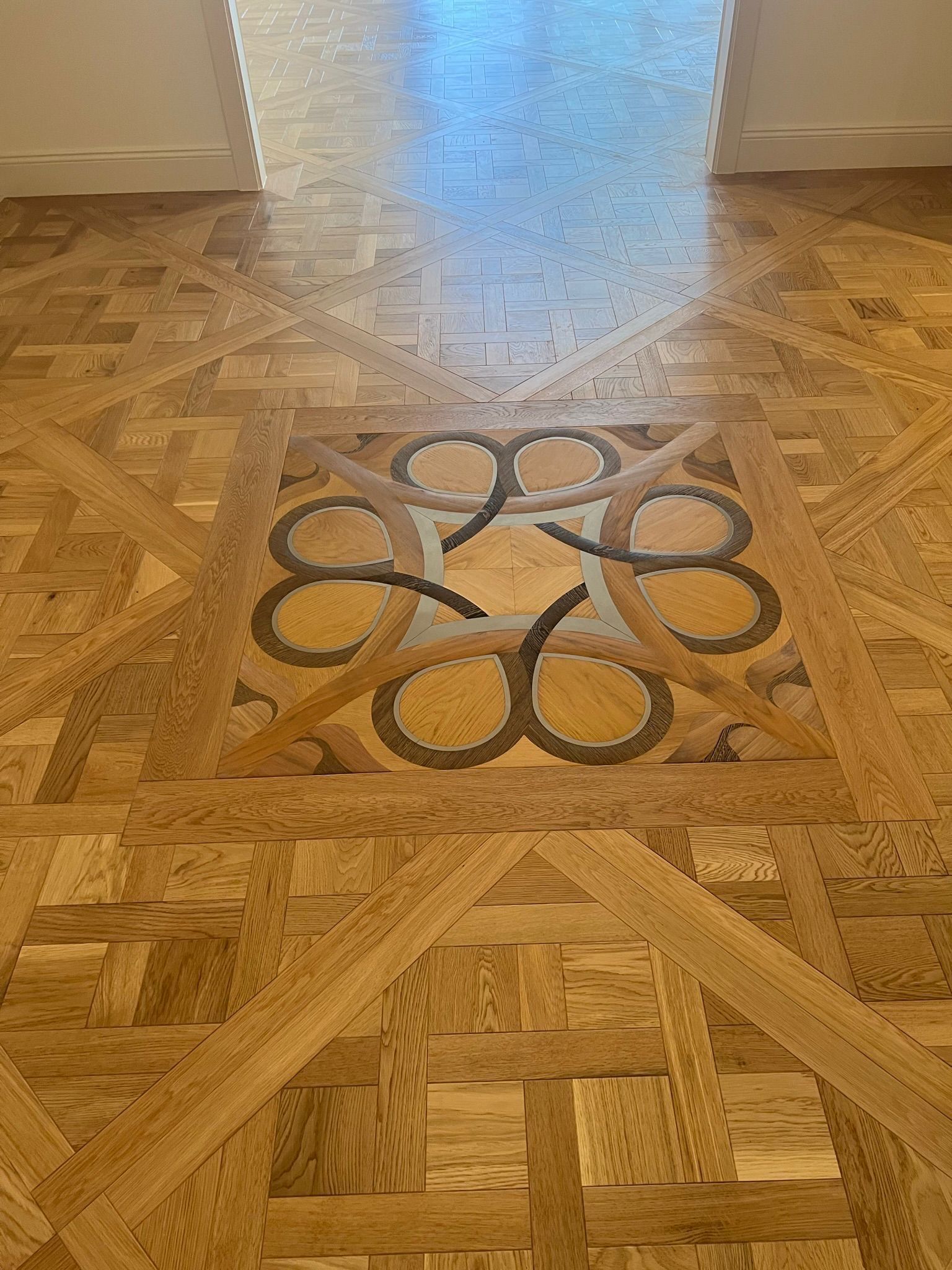 Parquet en bois finement travaillé, orné d'un médaillon carré à motif circulaire entrelacé, placé dans une entrée.