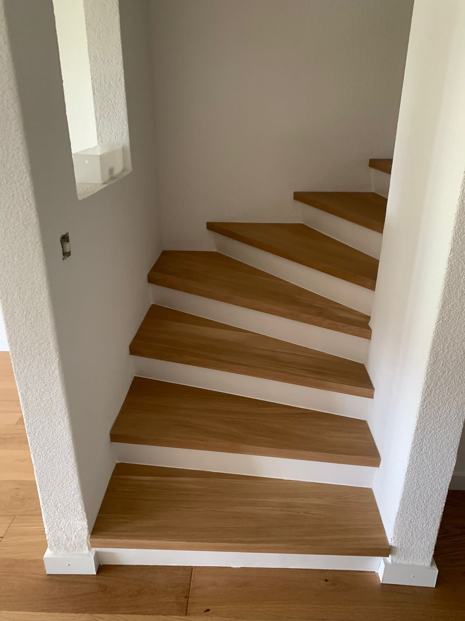 Escalier intérieur en bois avec contremarches blanches et murs texturés blancs dans un coin.