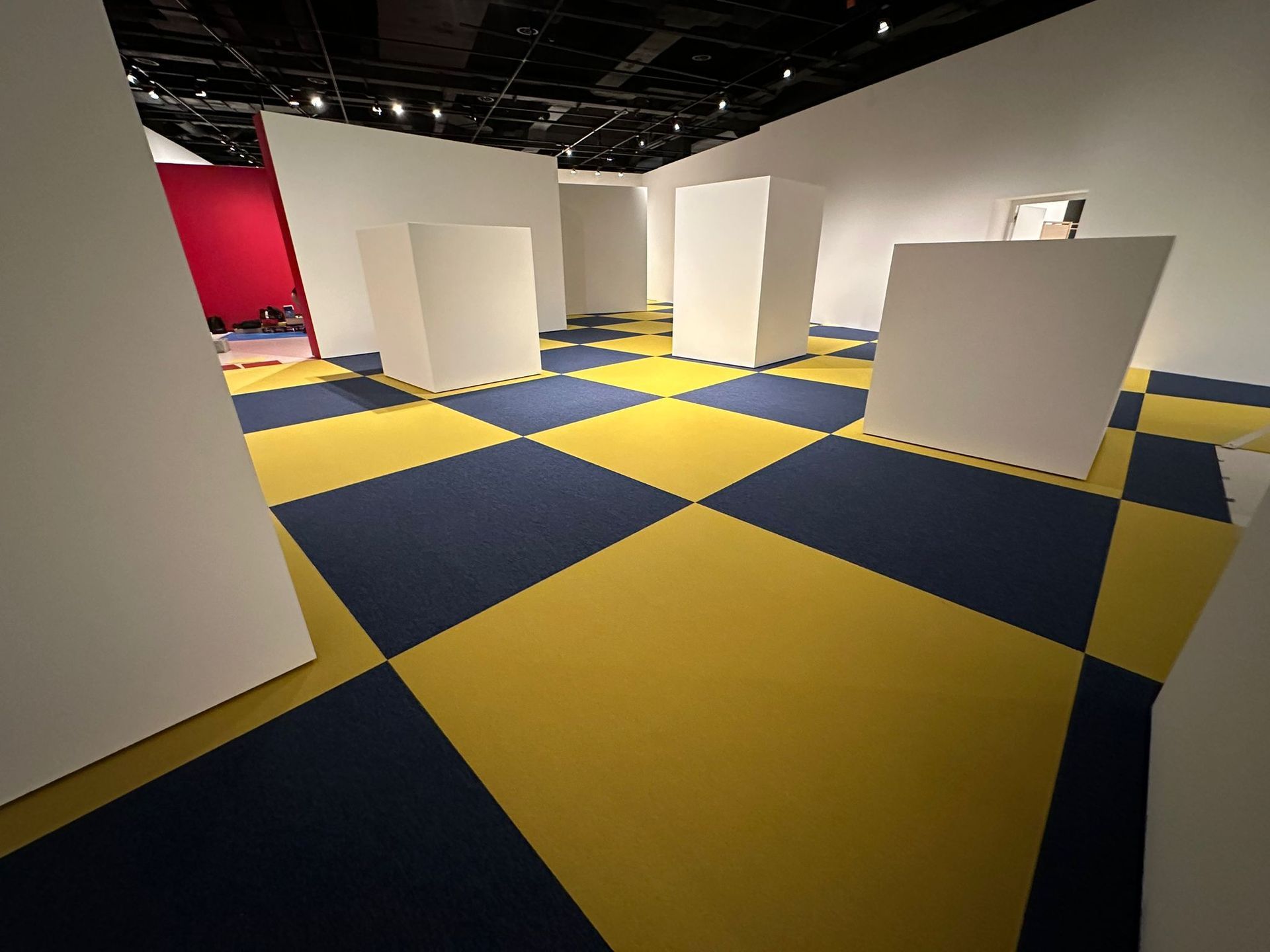 L'intérieur d'une galerie d'art avec des piliers blancs et un carrelage carré bleu et jaune à motif en damier.