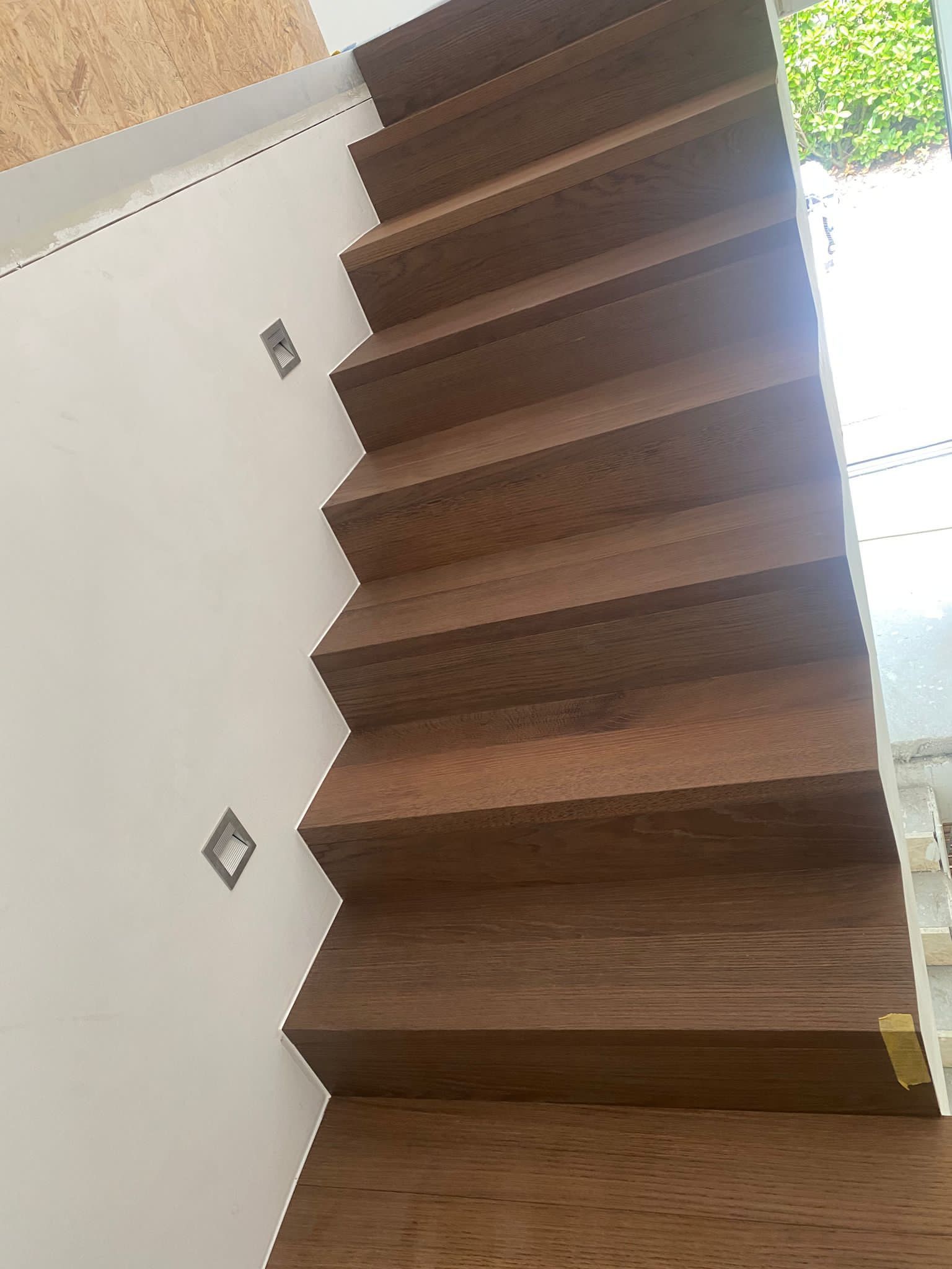 Escalier en bois foncé avec murs blancs, vue vers le haut et éclairage mural intégré.
