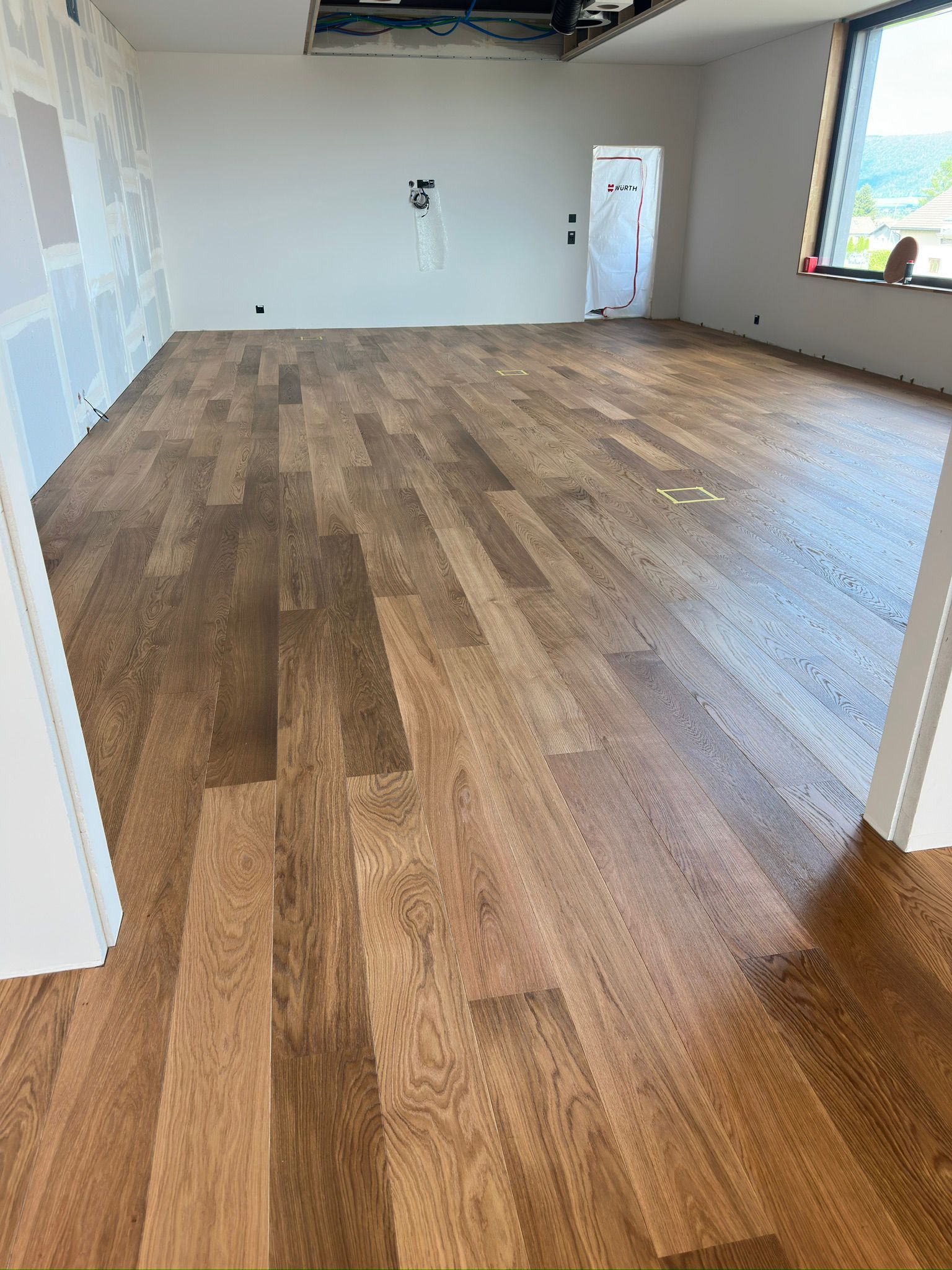Vue grand angle d'une pièce en rénovation avec un nouveau parquet, des murs clairs et une grande fenêtre.