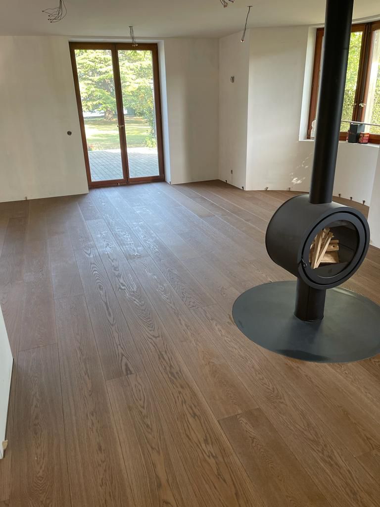 Une pièce minimaliste avec un parquet en bois brun clair, des murs blancs, de grandes portes-fenêtres vitrées et une cheminée circulaire moderne.
