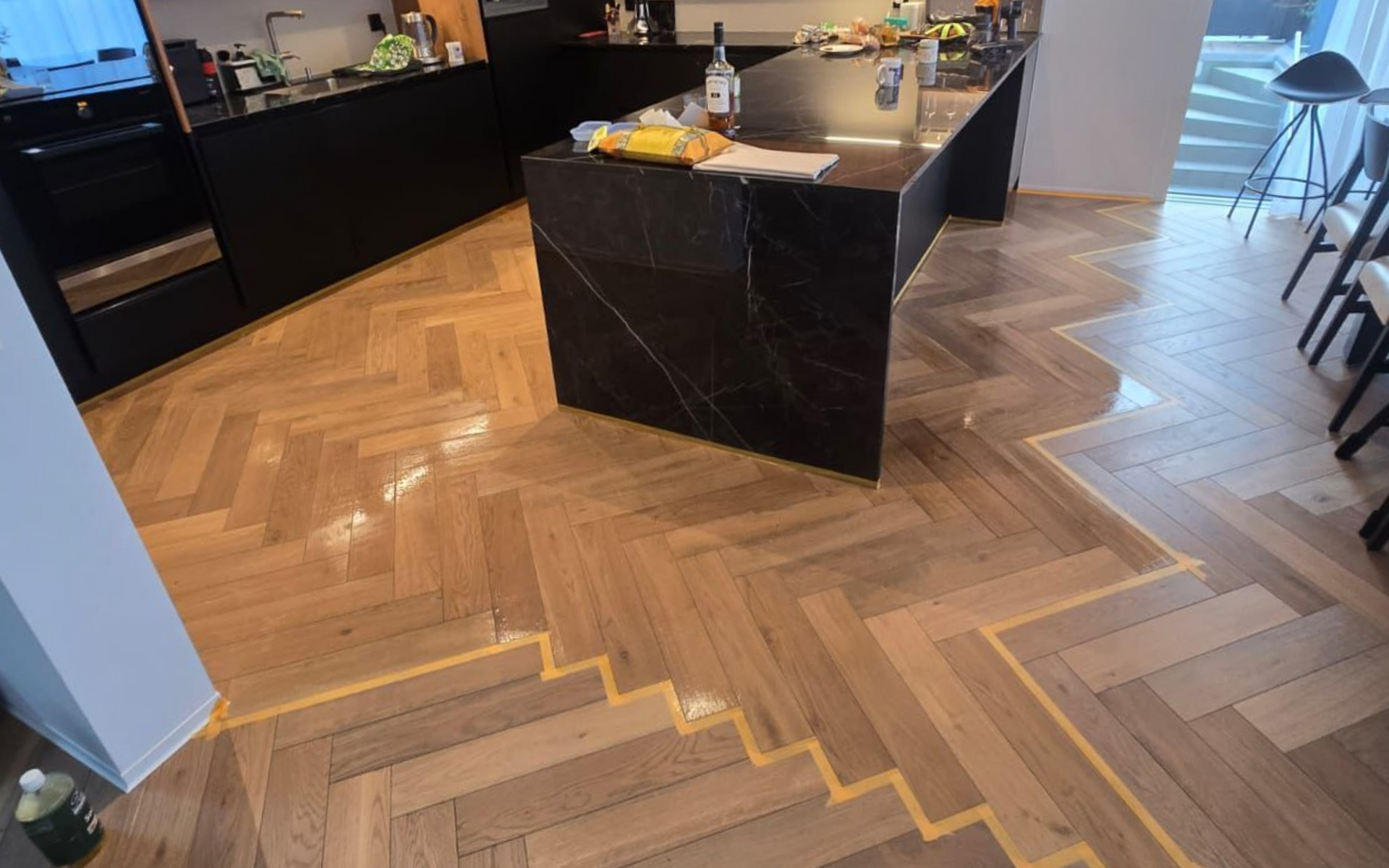 Plancher en bois à chevrons dans une cuisine, avec une ligne de transition diagonale marquée entre les parties en bois clair et foncé.