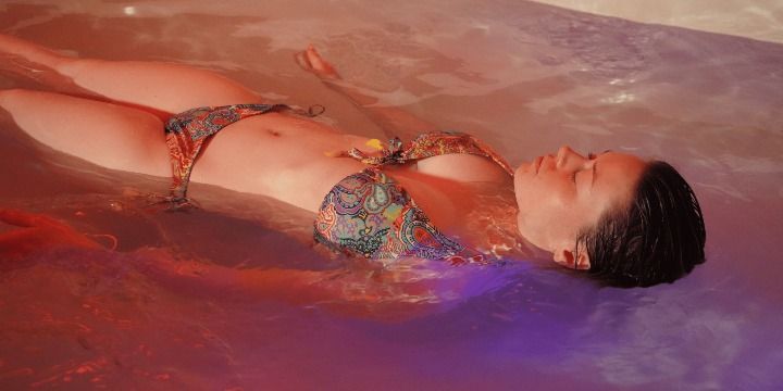 Woman floating on her back in purple-red water, wearing a colorful bikini.