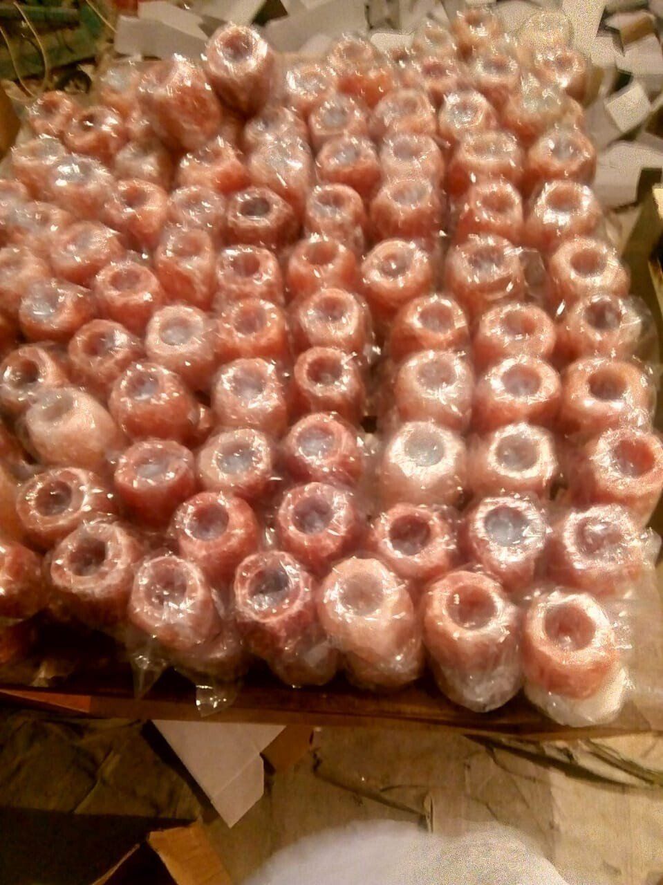 Many pink cylindrical items wrapped in clear plastic, stacked tightly in a tray, viewed from above