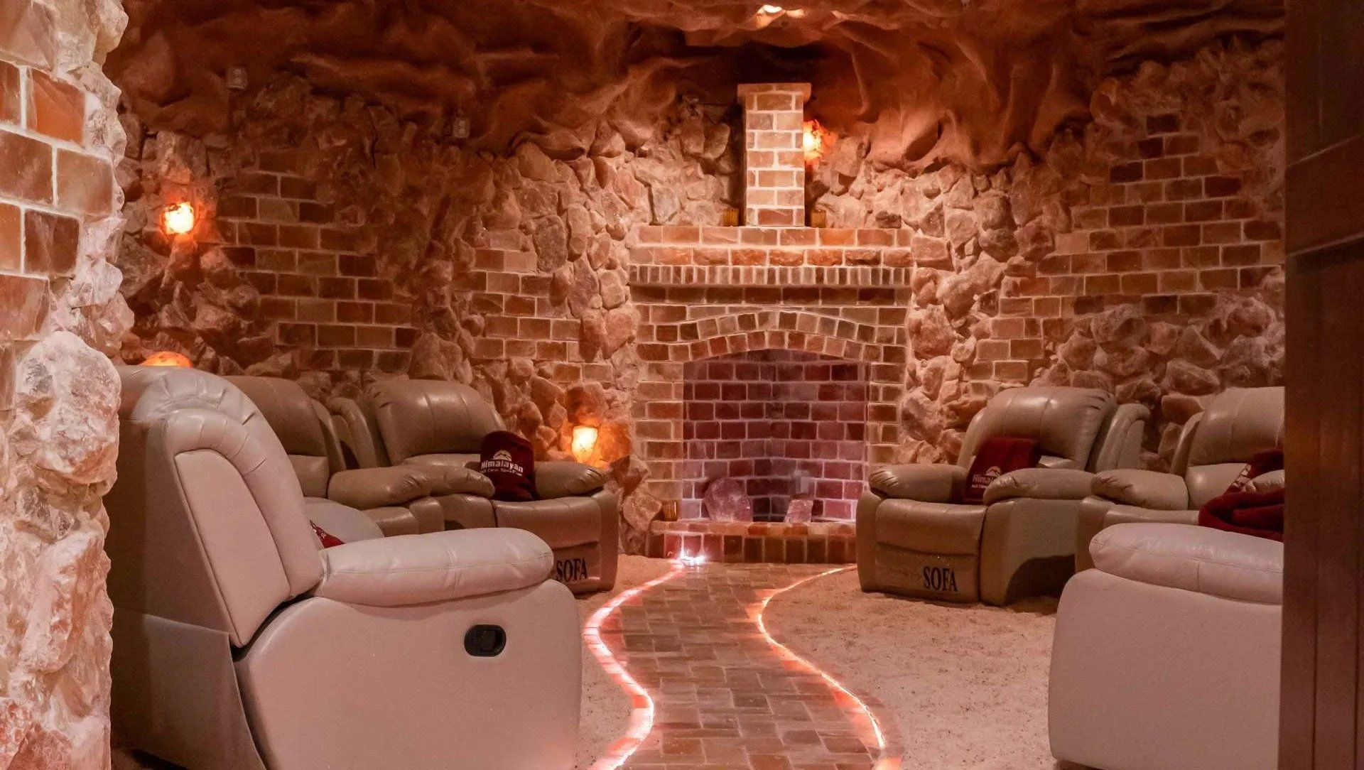 Stone-walled cozy lounge with reclining chairs, warm lighting, and a glowing path on the floor