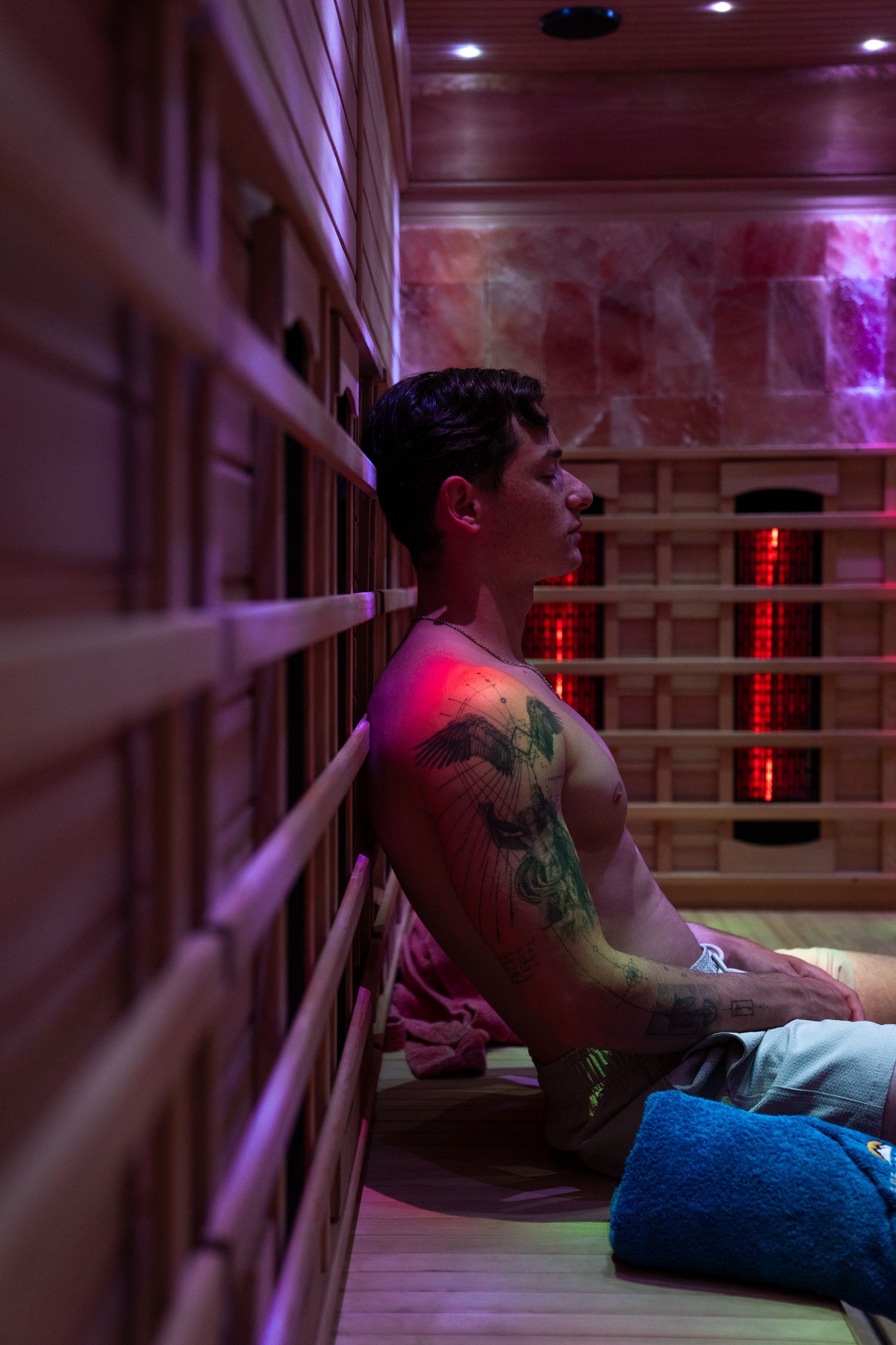Person reclining in a pink-lit sauna or steam room, leaning against wooden slats.