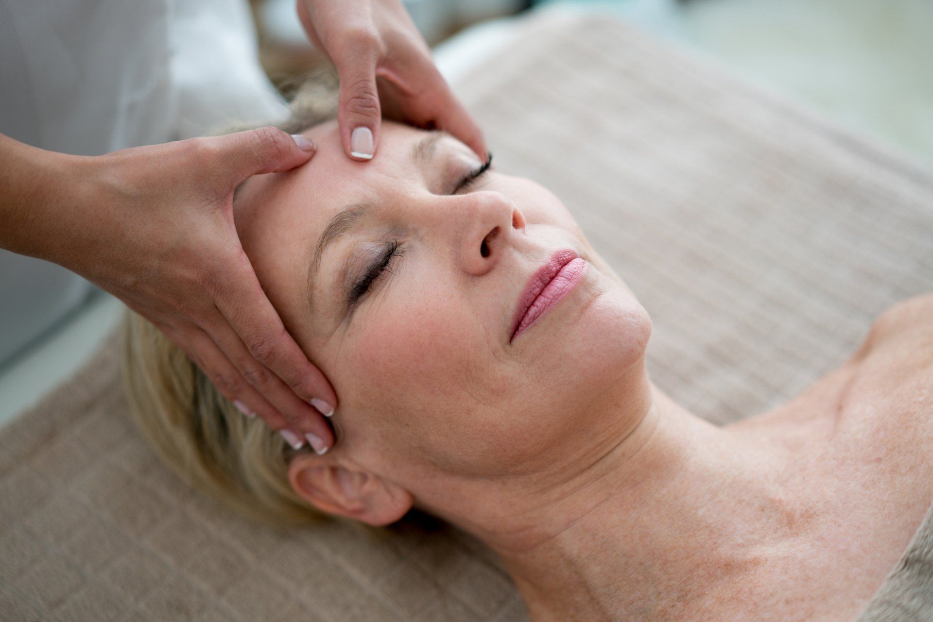 Woman receiving a facial massage with hands on her forehead. Eyes closed, relaxed expression.
