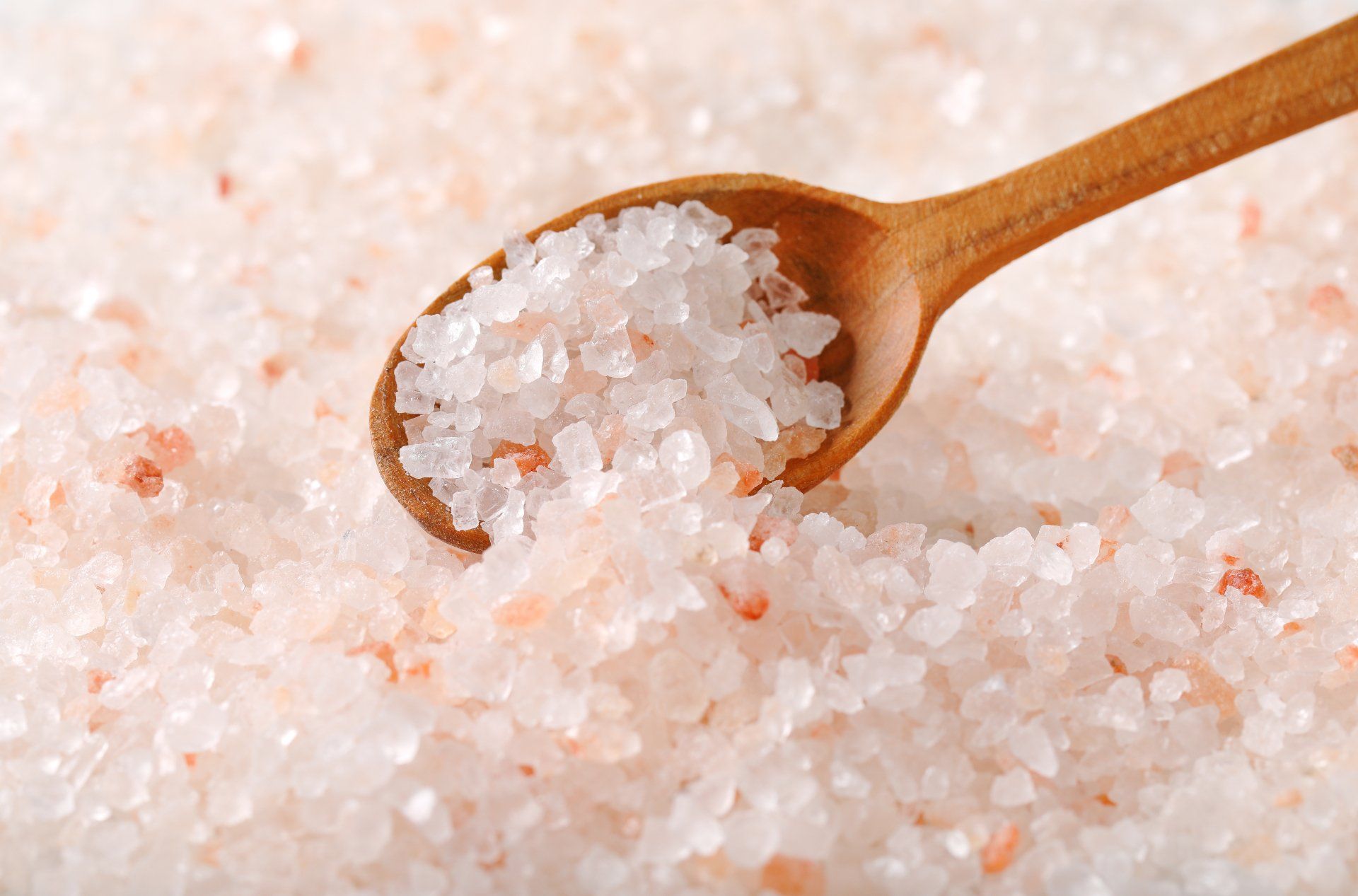 Wooden spoon scooping coarse pink salt crystals close-up