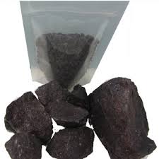 Transparent bag of dark, irregular rocks or ore pieces on a white background