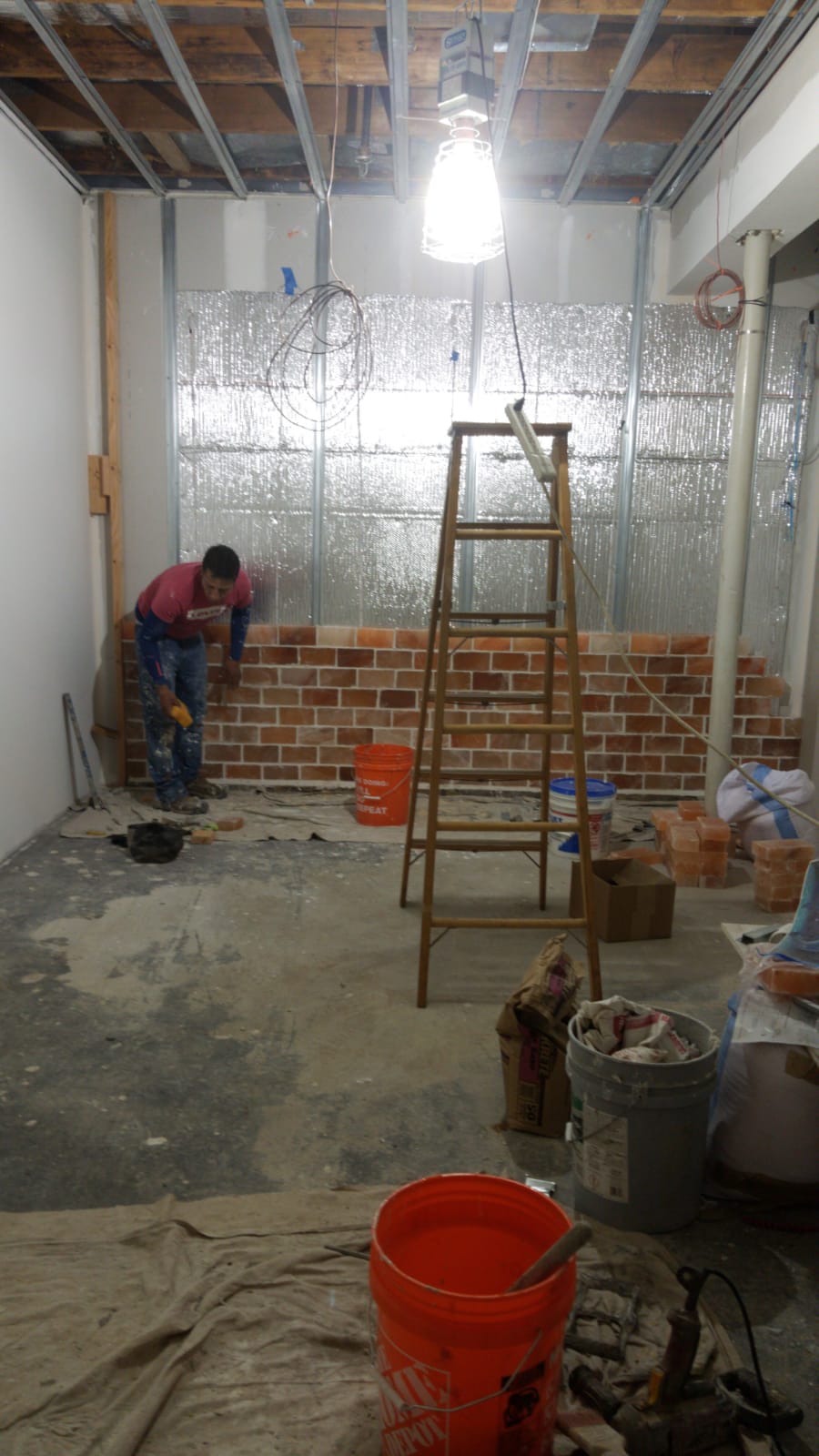 Partially renovated room with exposed ceiling, two workers, ladder, buckets, and construction debris