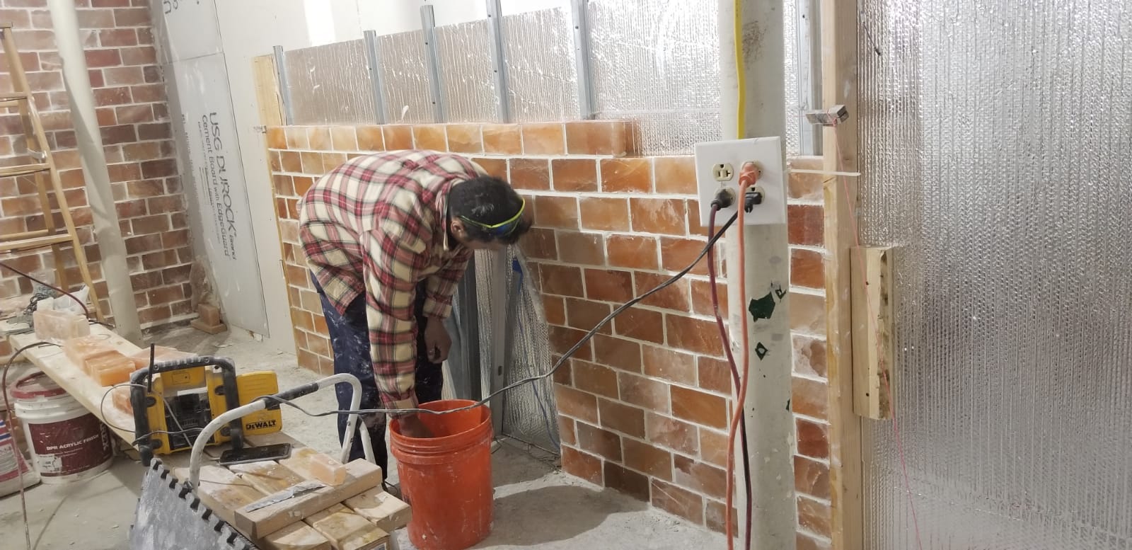 Worker plastering a brick wall at a construction site, with tools and buckets nearby.
