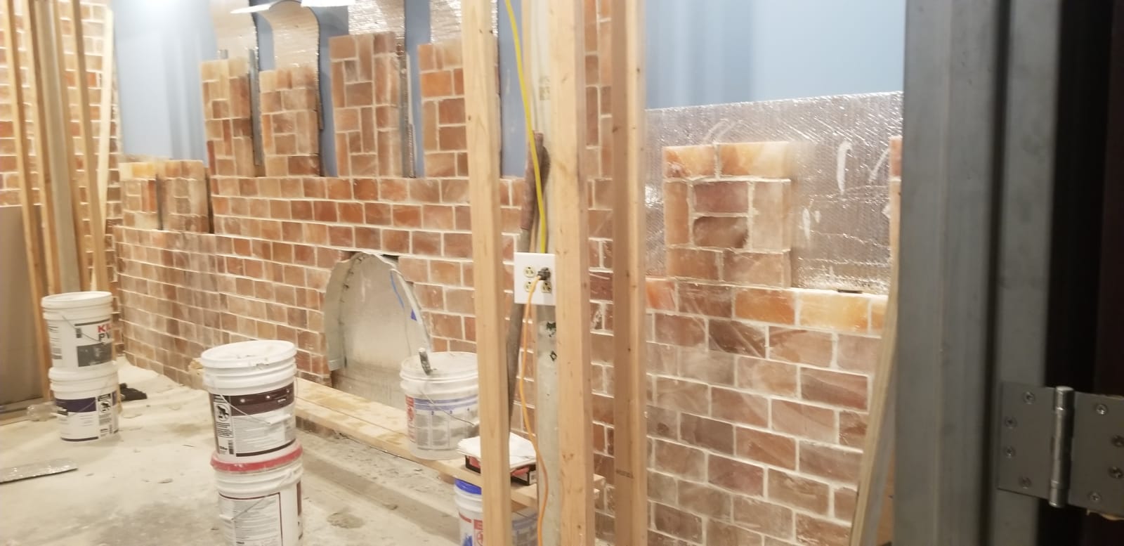 Partially built brick wall inside a workshop, with buckets and tools in front of it.