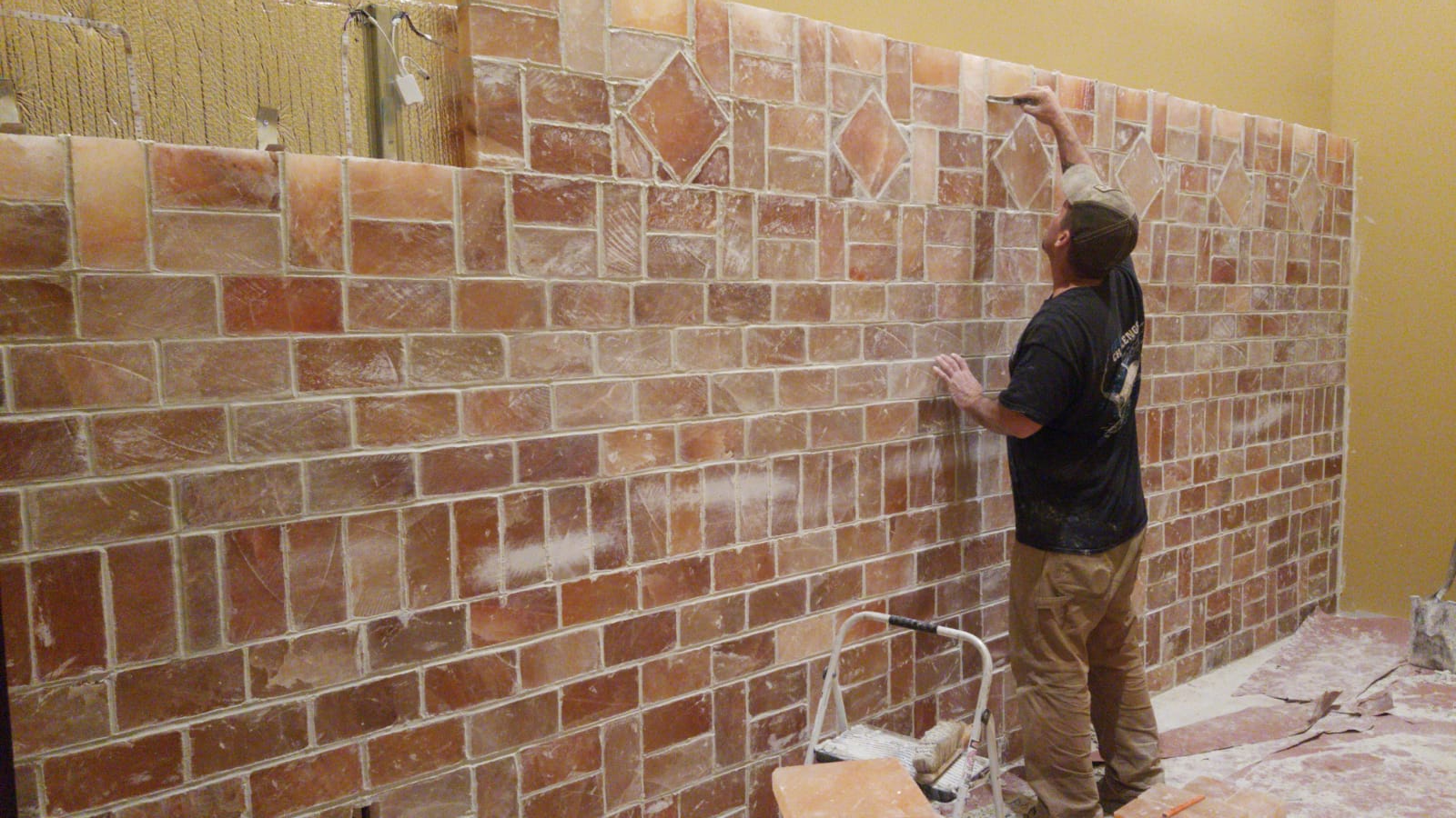 Person applying reddish tiles to a wall in a room under construction