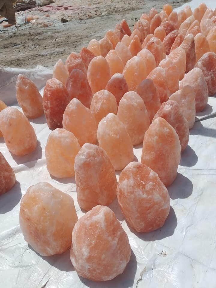 Rows of pink-orange Himalayan salt crystals drying on a white sheet outdoors.