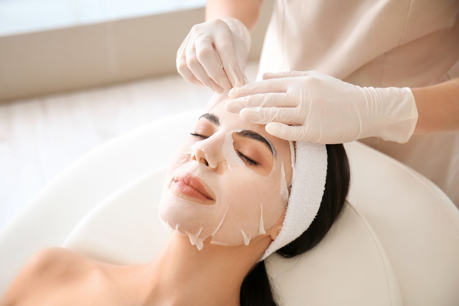 Facial treatment with gloved hands applying cream to a woman’s face in a spa setting