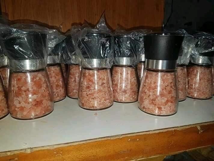 Rows of pink salt grinders with black caps arranged on a shelf, wrapped in plastic.
