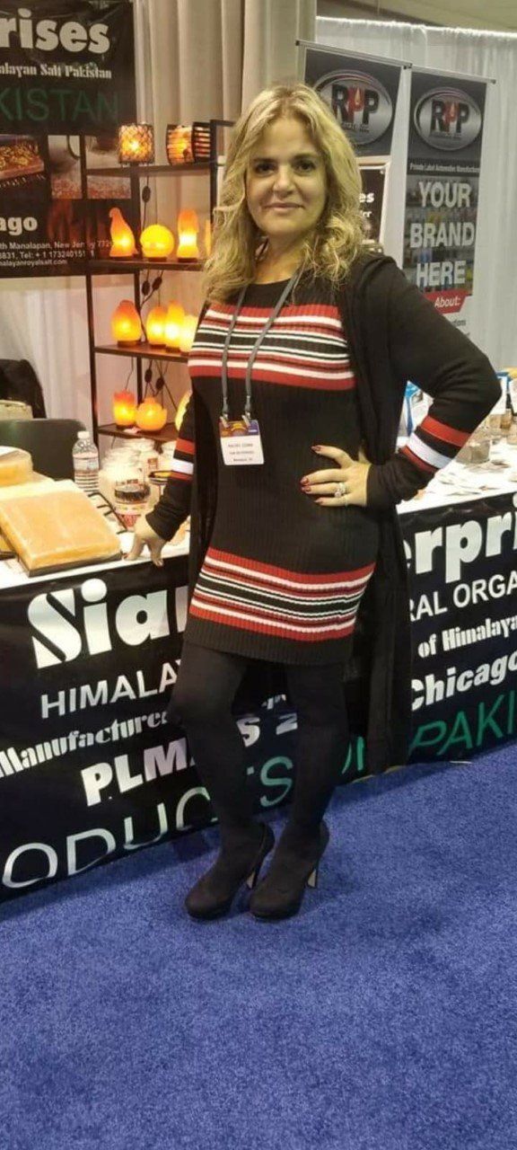 Woman posing at a trade show booth, wearing a black and red striped dress and black cardigan.