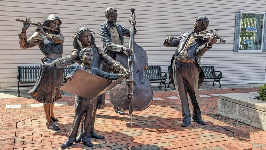 Four bronze musicians playing instruments on a brick plaza beside a building