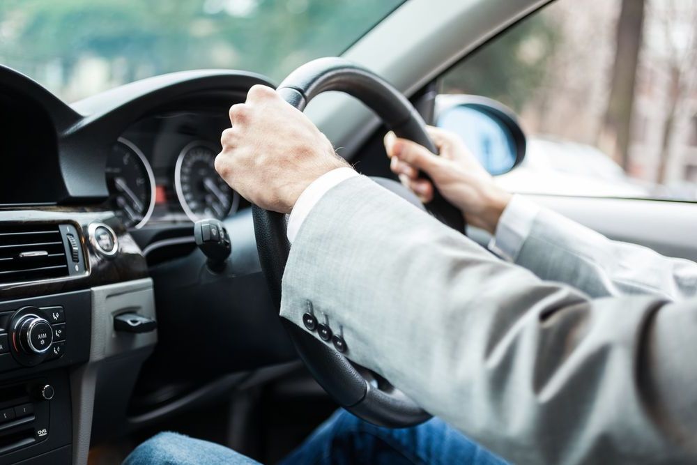 A Man In A Suit Is Driving A Car — Spencer Lawyers In Gosford, NSW