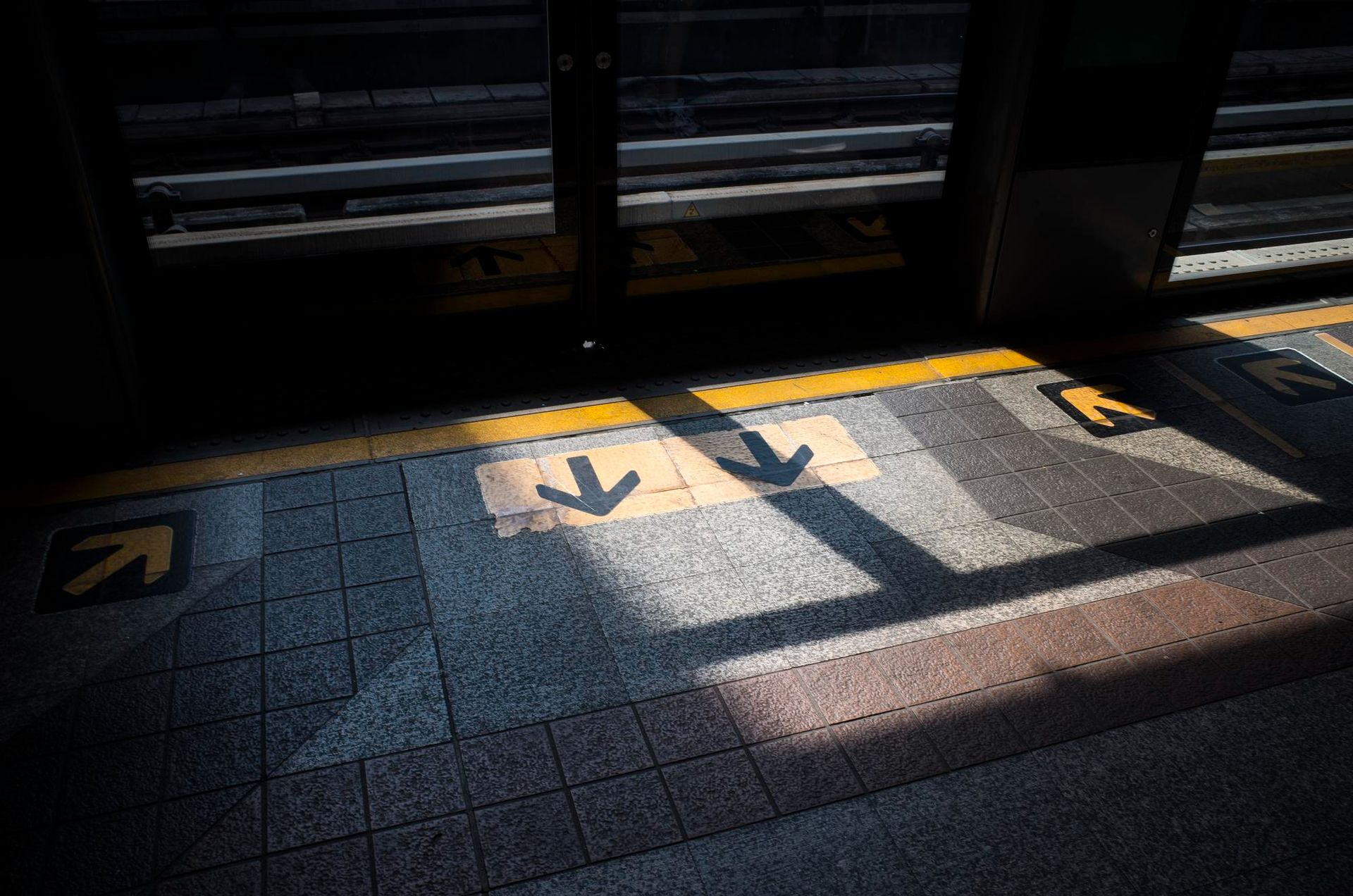 Platform edge with yellow arrows, sunlight casting shadows.