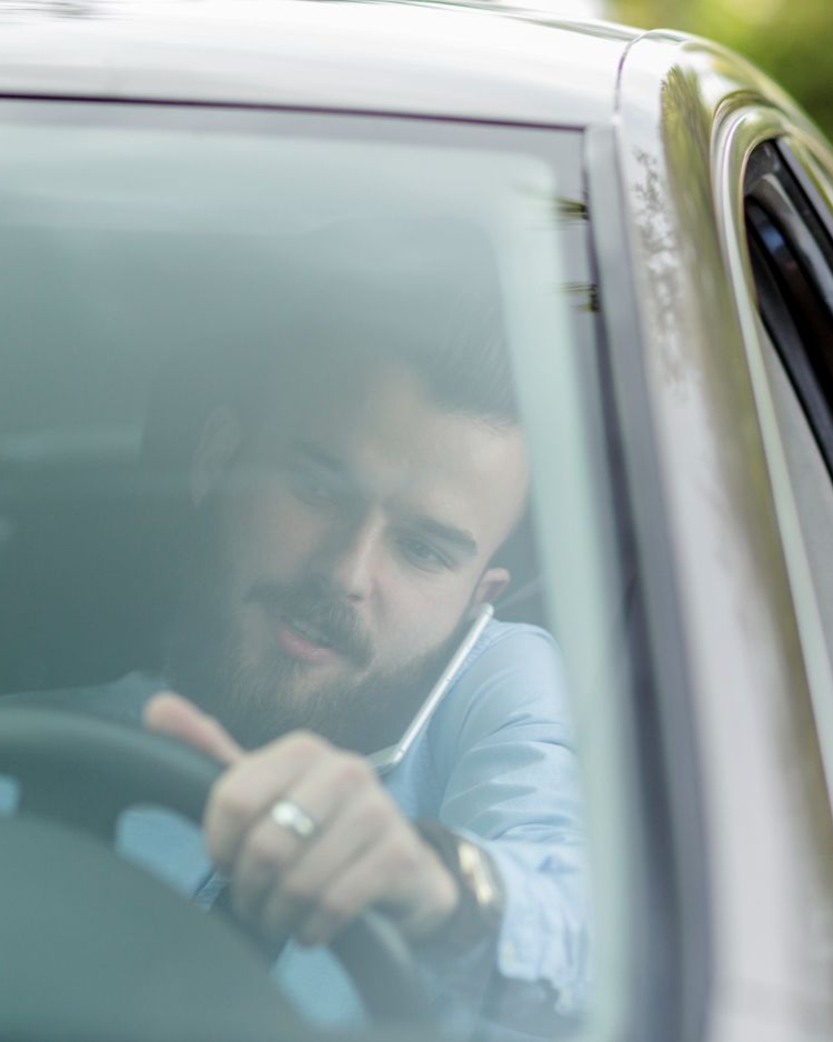 Man driving and talking on a cell phone, seen through the car's windshield.