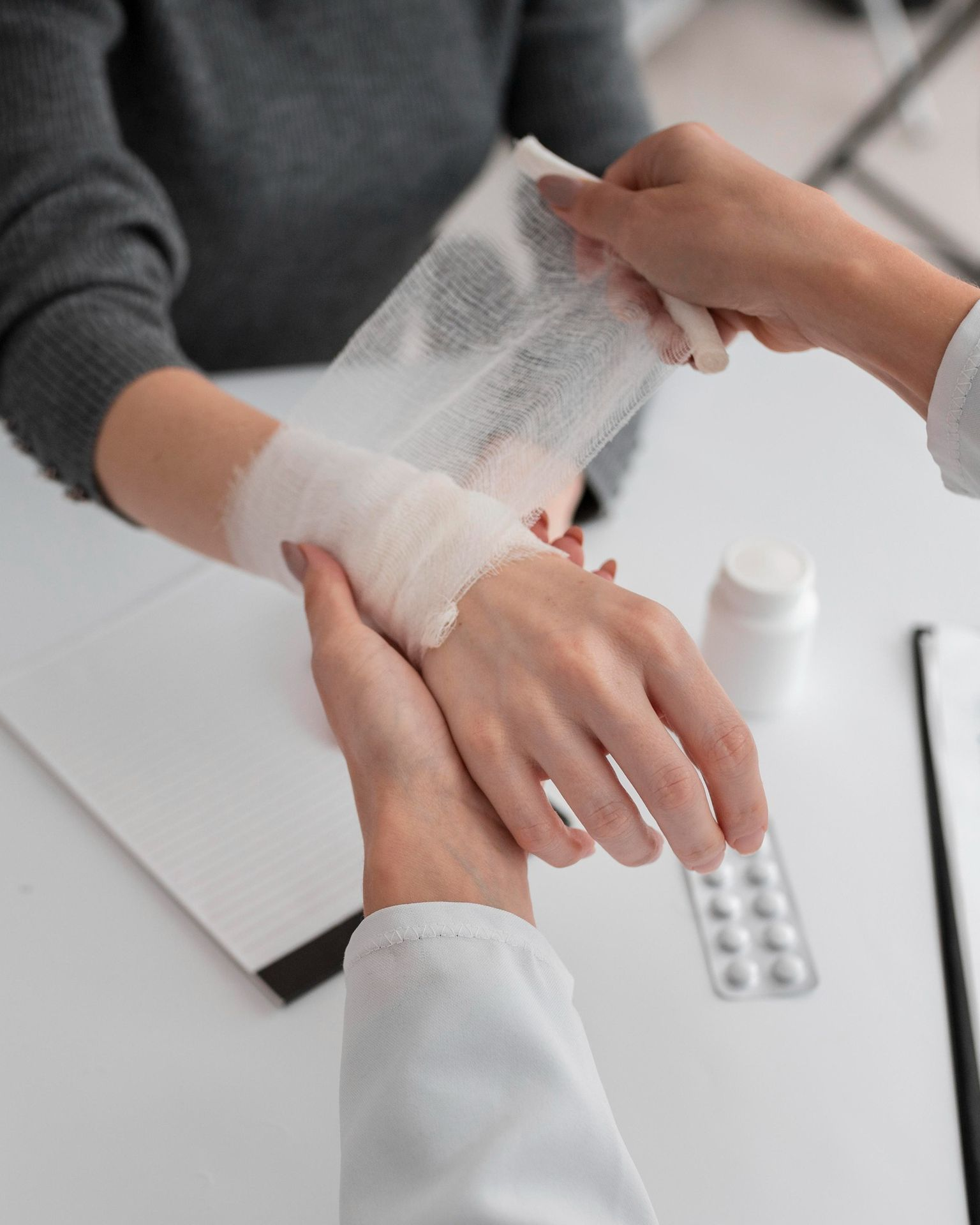 Doctor wrapping a bandage around a patient's injured wrist in a medical setting.