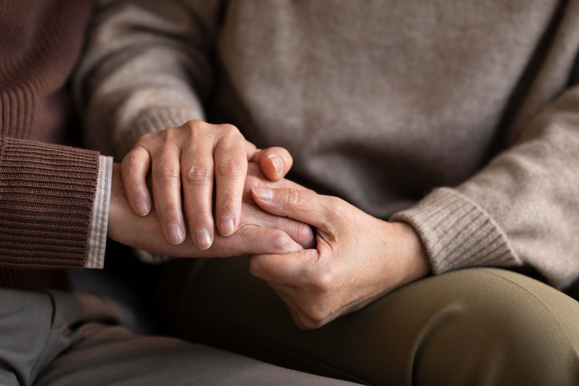 Person's hand gently holding another's, both wearing sweaters, conveying comfort.