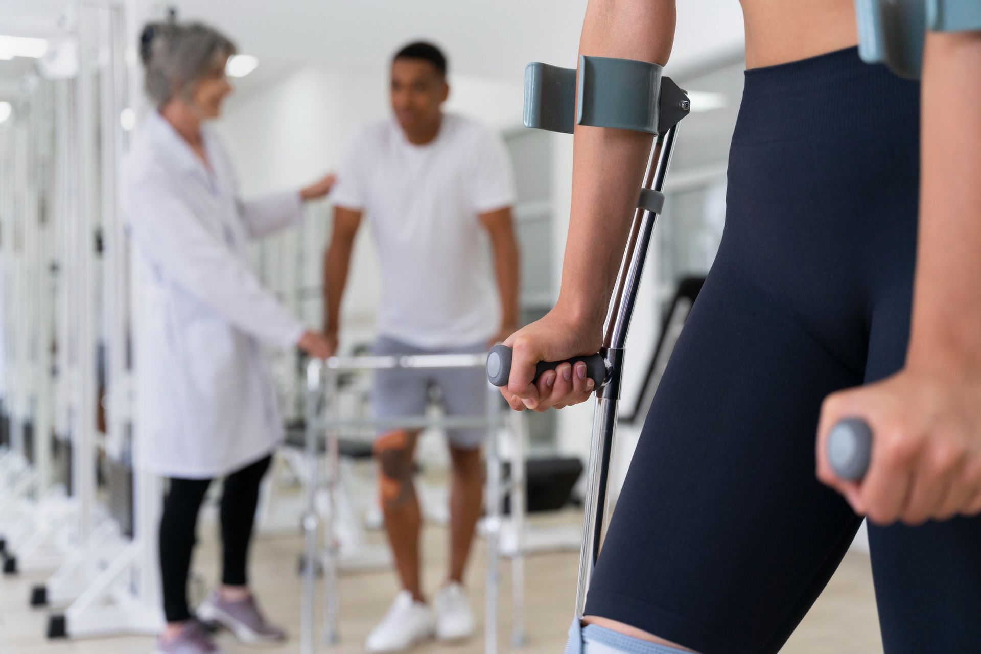 Woman with crutches in a therapy session; therapist and patient with walker in the background.