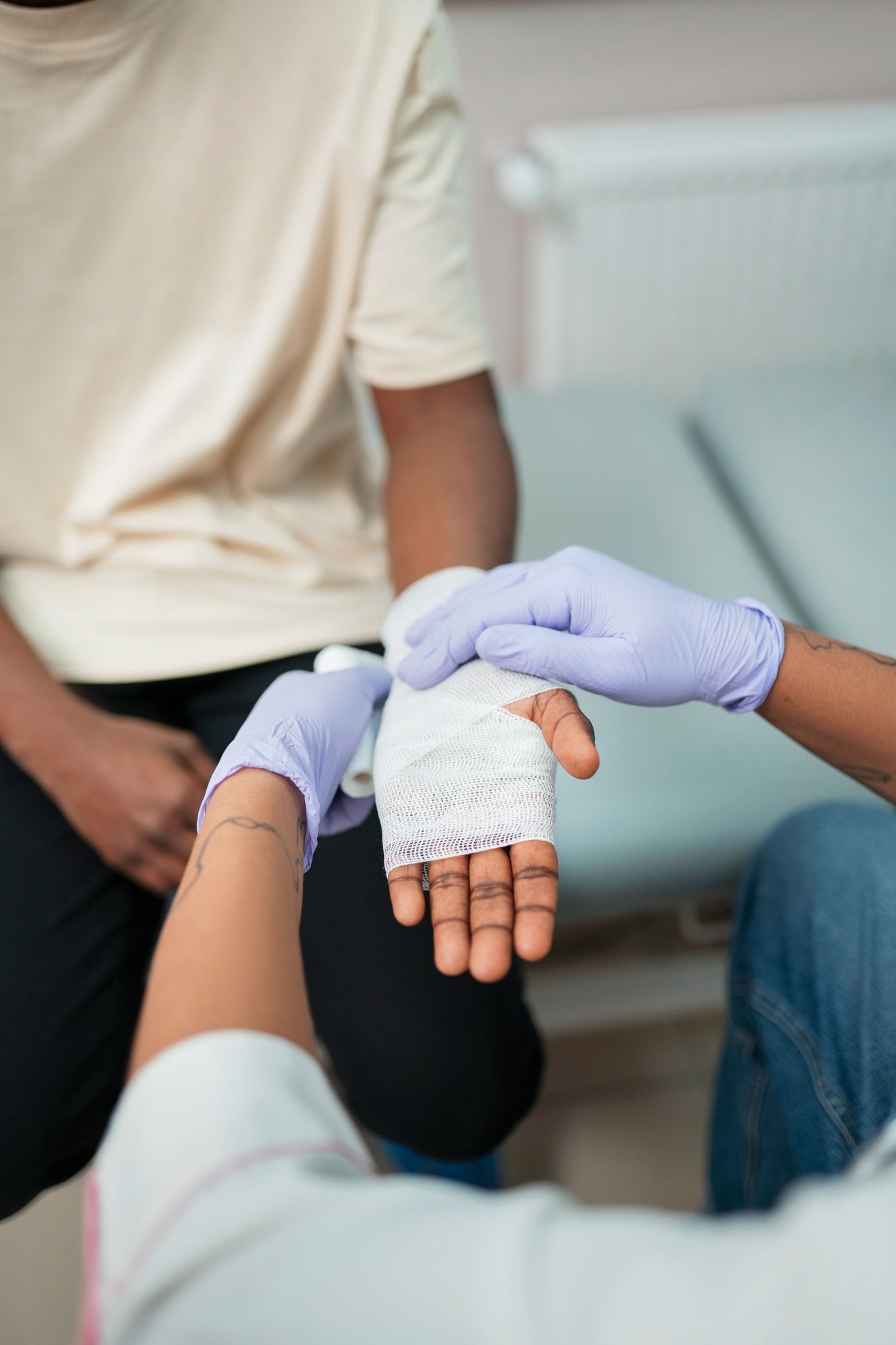 Person's bandaged hand held by another with gloved hands; interior setting.