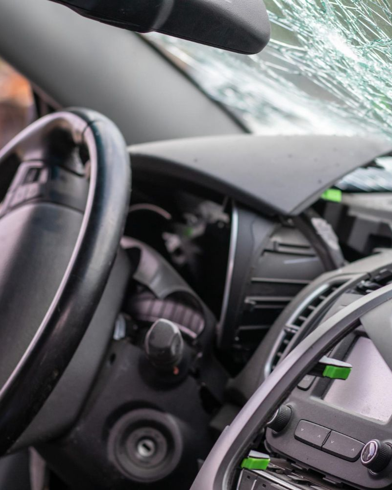Interior of a car; cracked windshield, dashboard damage, steering wheel visible.