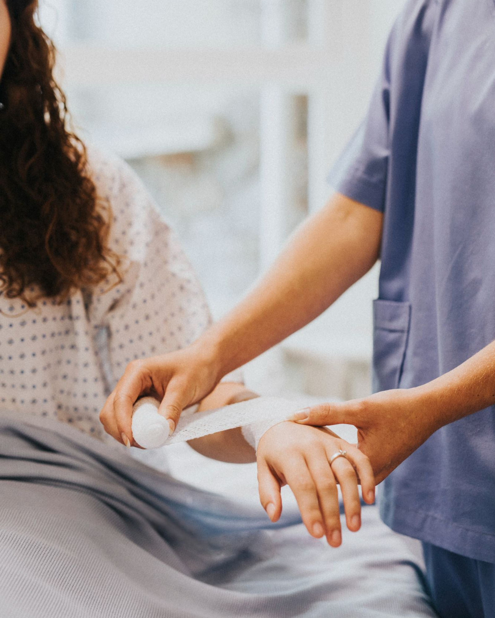 Nurse wrapping a patient's wrist with a bandage in a medical setting.