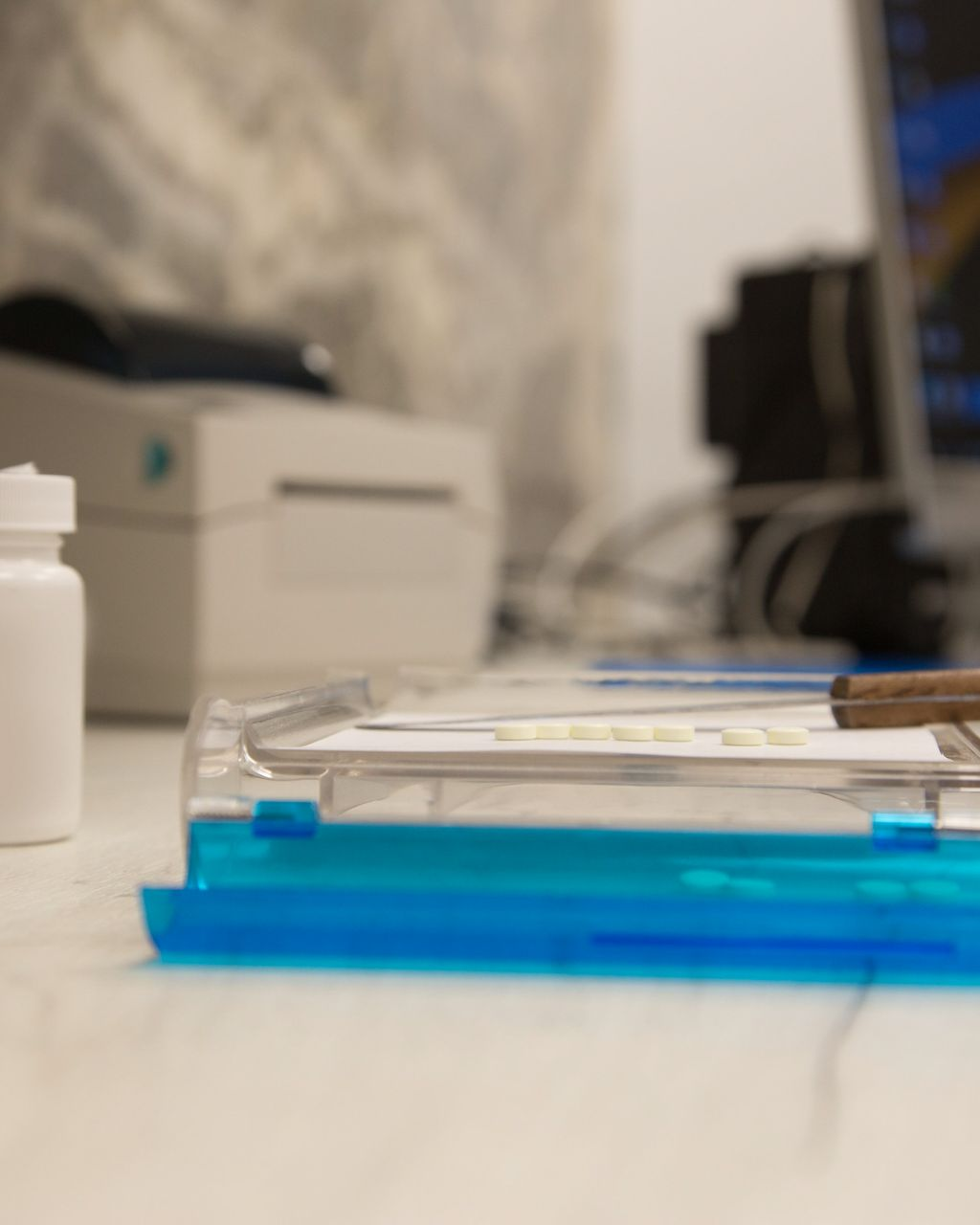 Blue medical tray on white table with a printer, bottle, and computer in the blurred background.