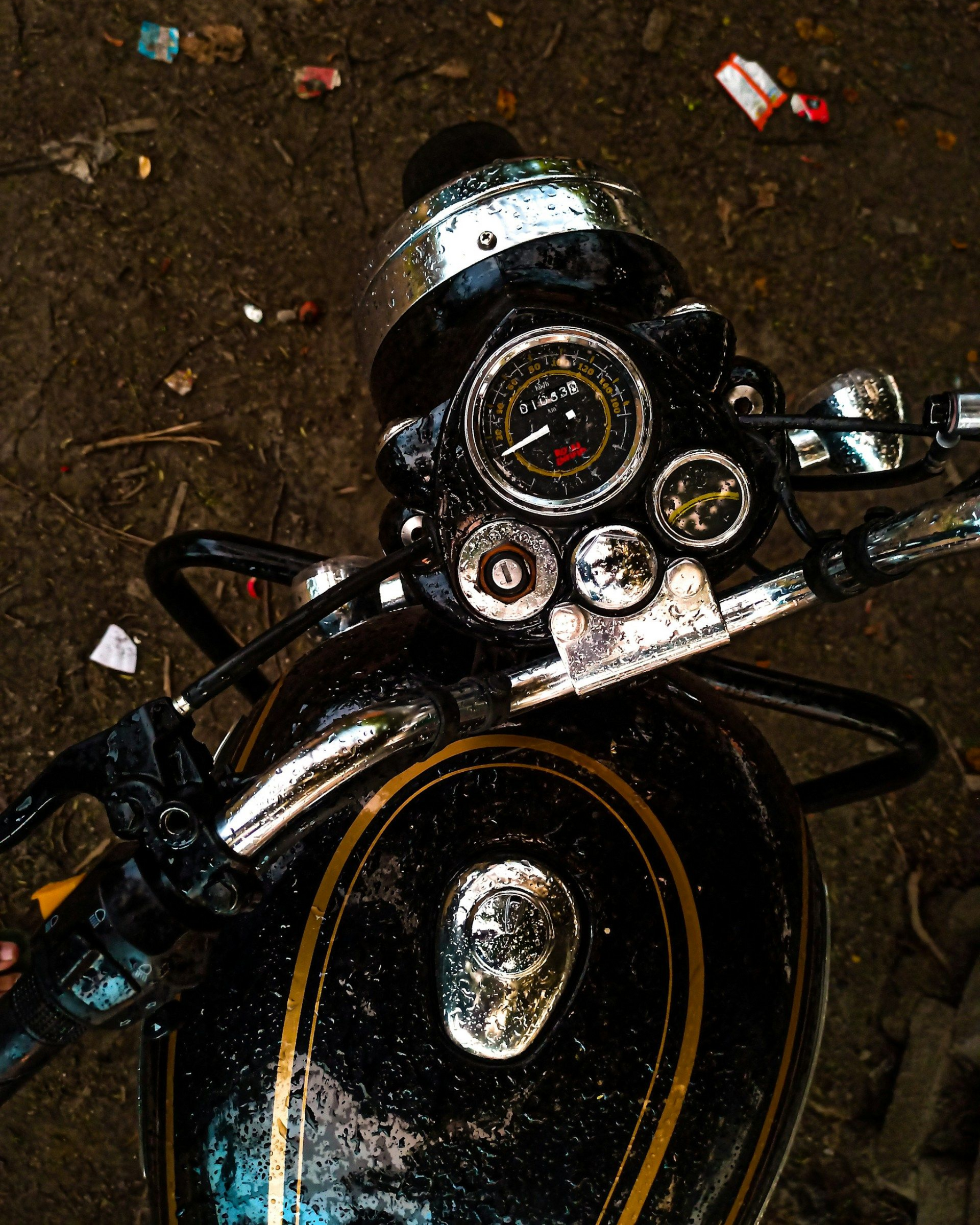 Black and gold Royal Enfield motorcycle with chrome details, viewed from above, on a muddy surface.