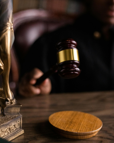Judge holding a gavel in court, striking the sound block; Lady Justice statue visible.
