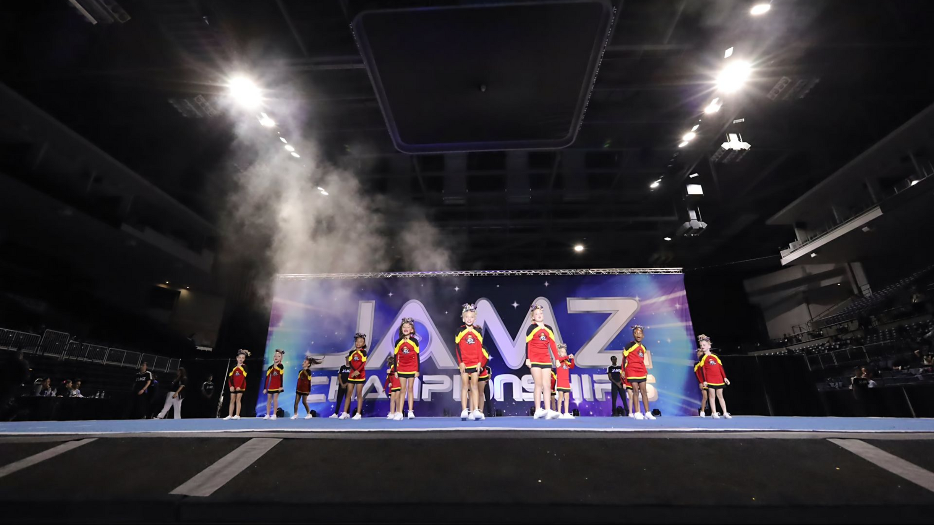 Performers on a stage with bright lights and a large screen backdrop reading “MIZ”