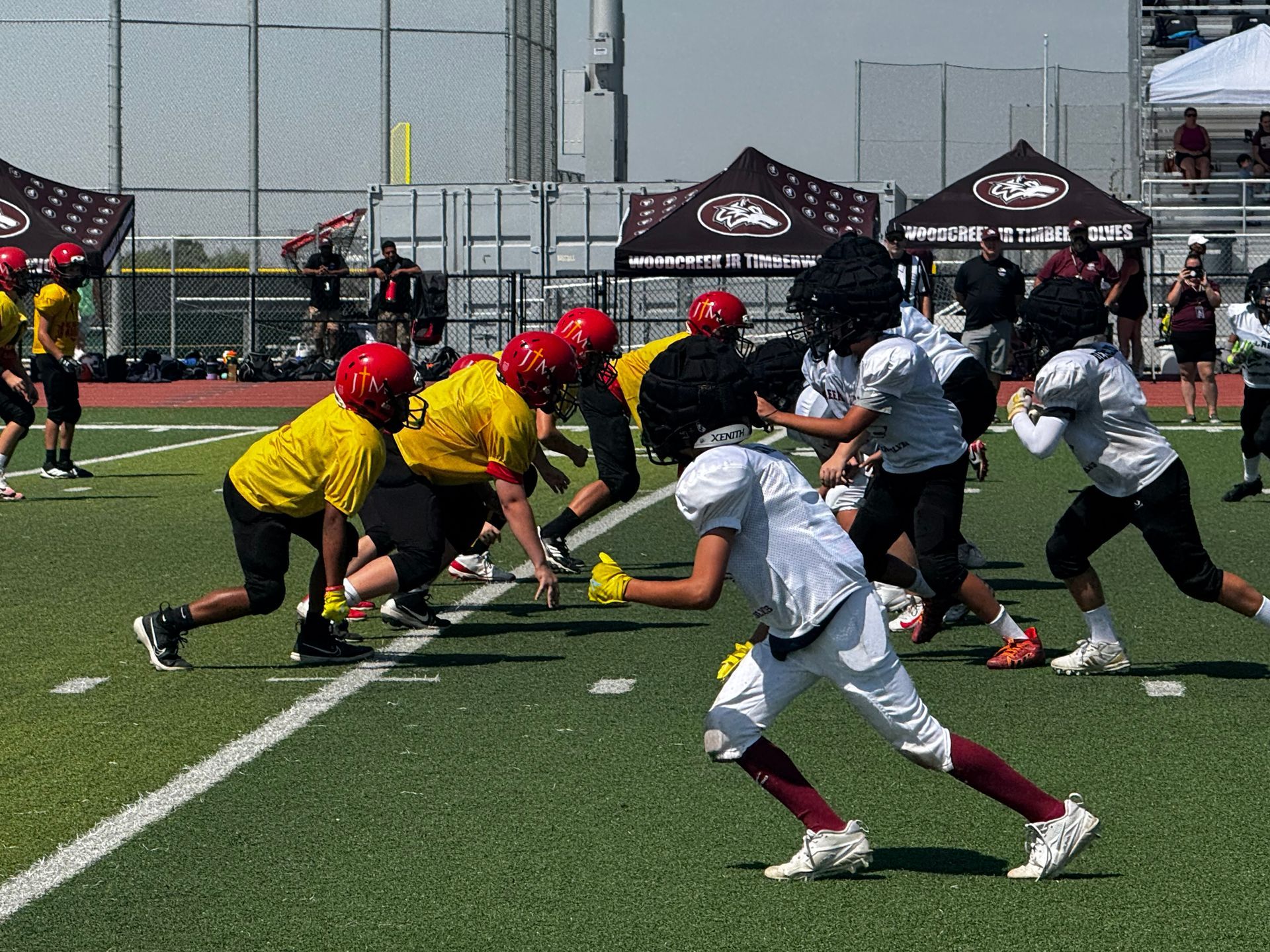 Youth football players in yellow and white uniforms line up at the snap on a field.