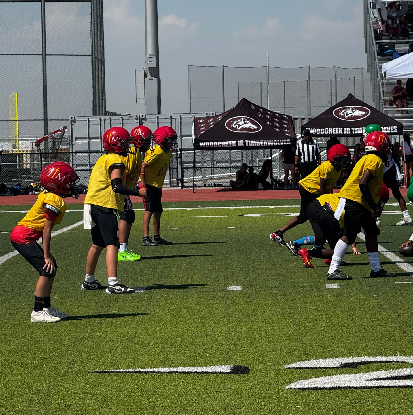 Youth flag football players in red helmets and yellow jerseys line up on a turf field.
