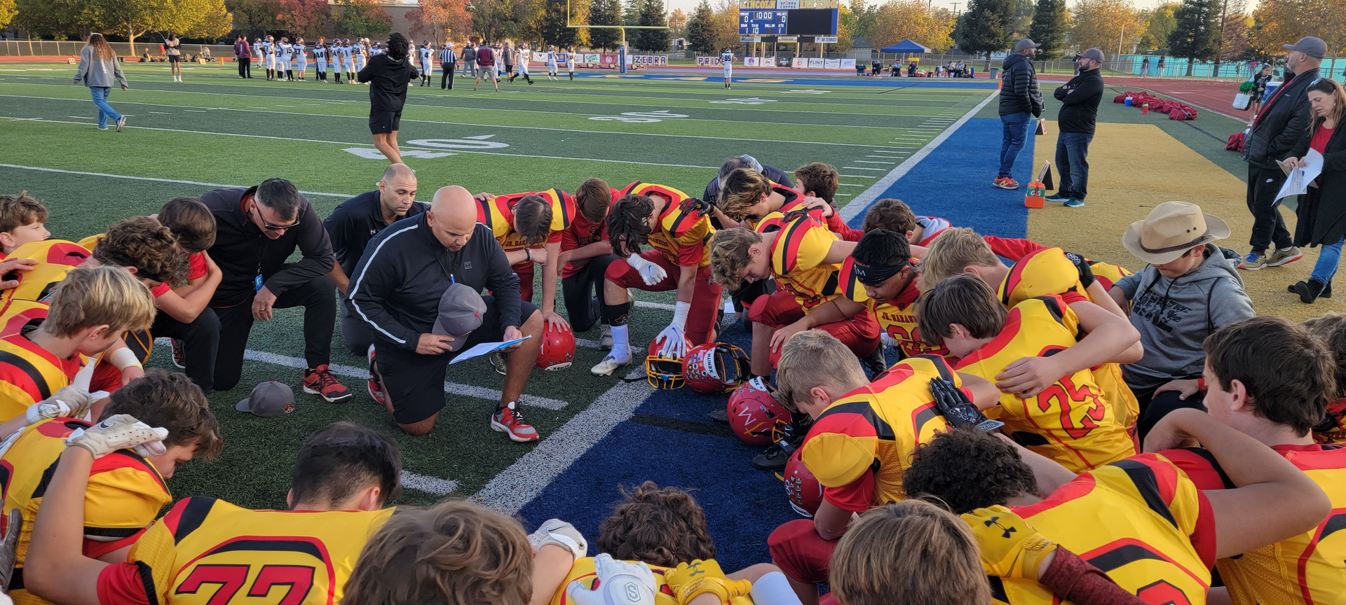 Football team huddled on the field around a coach during a pregame pep talk at dusk