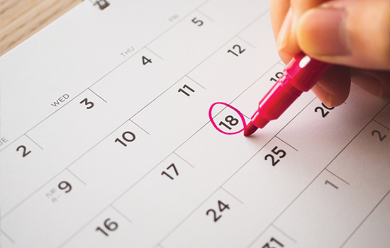 Hand circling the 18 on a calendar with a red marker