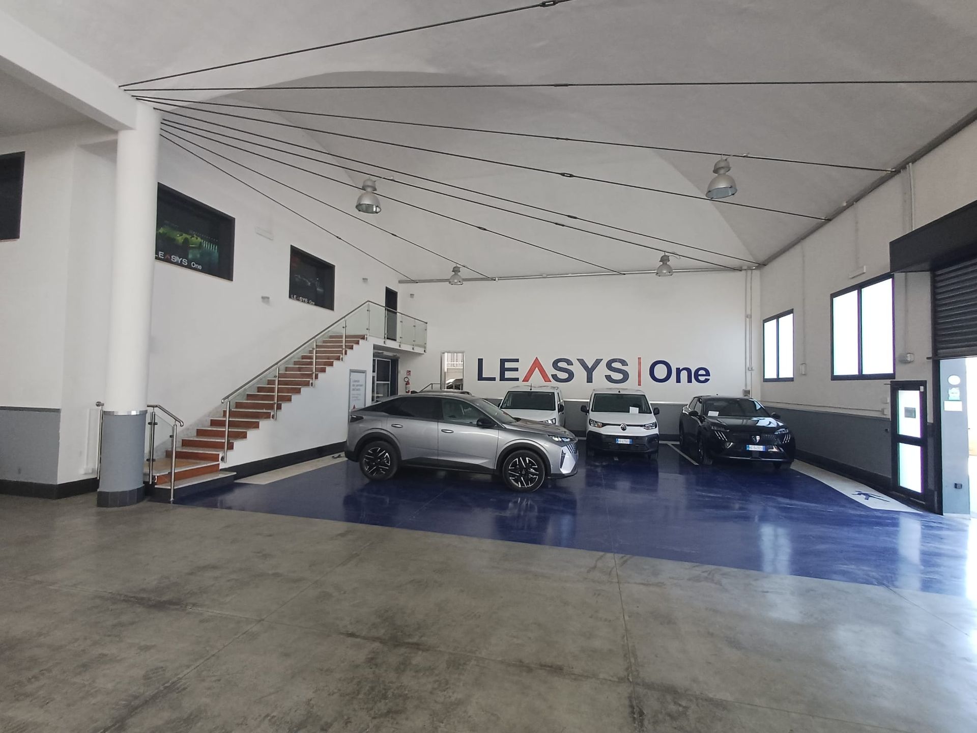 Ampio showroom con tre auto, una scala e il marchio