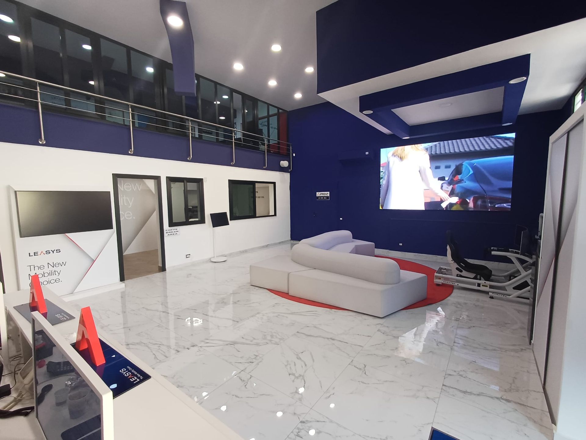 Soggiorno moderno con pavimento bianco lucido, parete d'accento blu, grande televisore e divano componibile grigio.