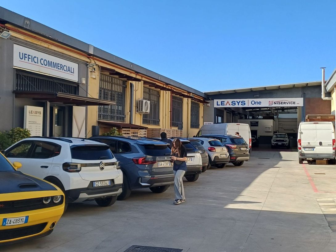 Un meccanico in tuta blu lavora sotto una Volkswagen nera sollevata in un'officina di riparazione auto.